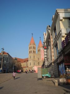 Das Foto zeigt die Kathedrale in Qingdao und den davor gelegenen Platz vor stahlblauem Himmel.